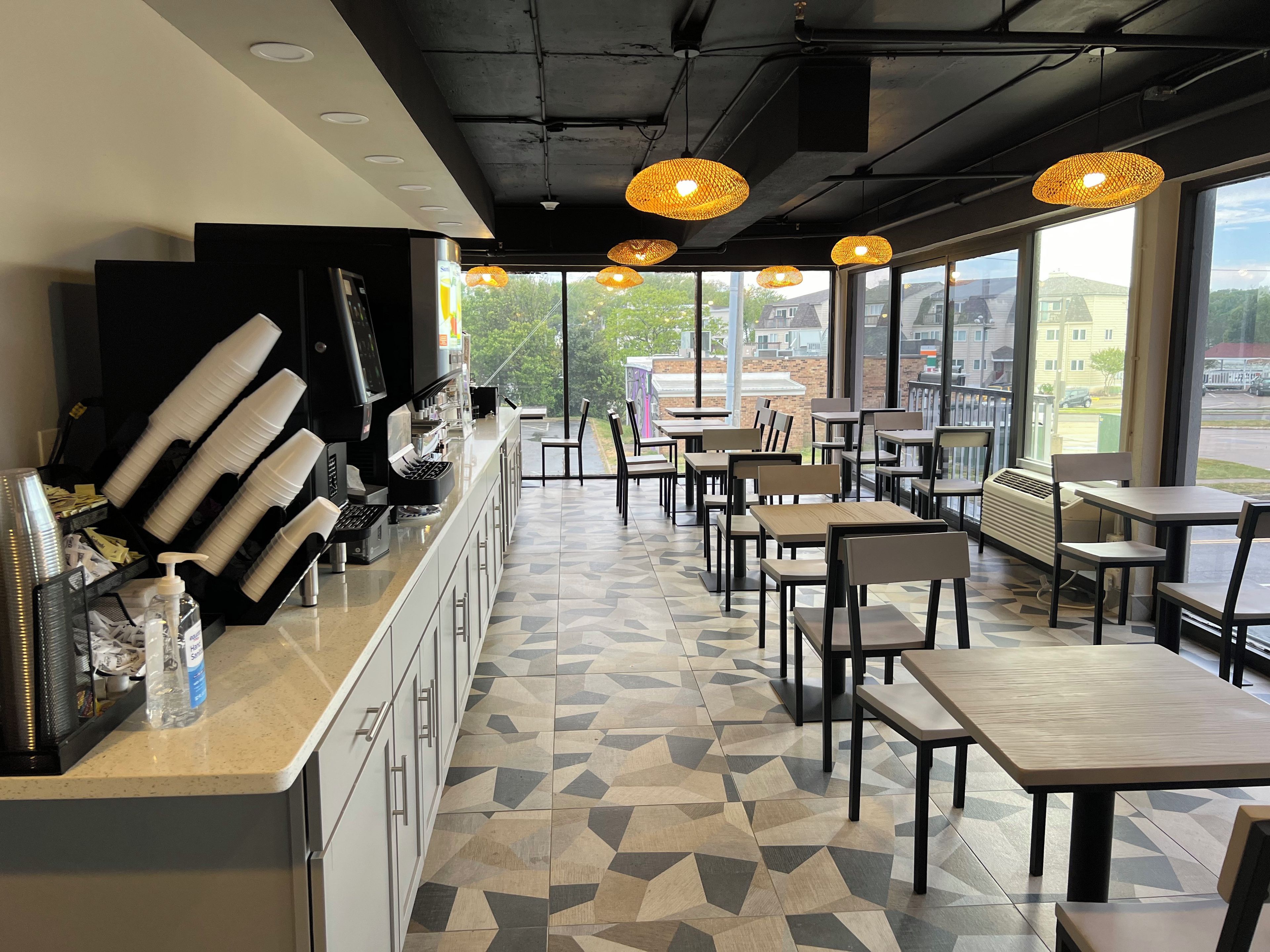 A cafe with a long counter, chairs, tables, and large windows offering a view of the outside.