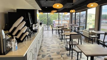 A cafe with a long counter, chairs, tables, and large windows offering a view of the outside.