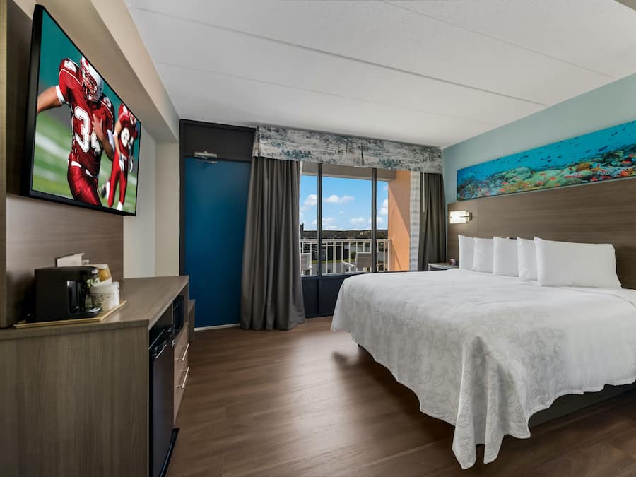 A hotel room with a large bed, a television on the wall, and a painting of an underwater scene.