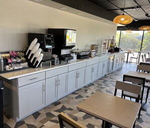 A modern cafe with a long counter, coffee machines, and seating area. - Red Roof Inn PLUS+ & Suites Virginia Beach – Seaside (Virginia Beach)