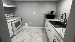 Cozinha compacta com fogão branco, micro-ondas preto e pia de aço inoxidável.