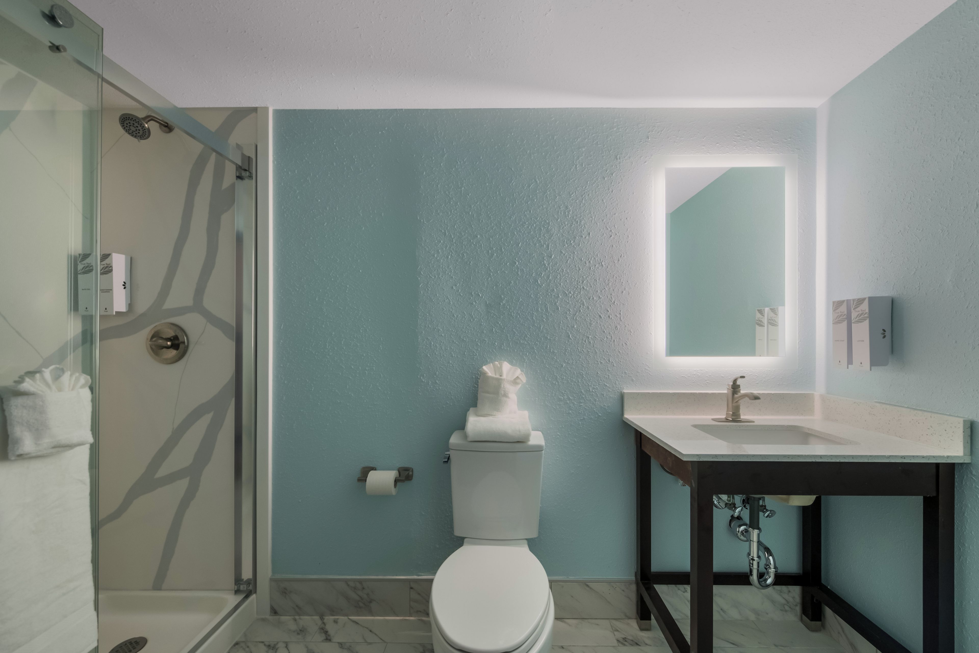 A modern bathroom with a glass-enclosed shower, a white toilet, a sink with a mirror, and marble flooring.