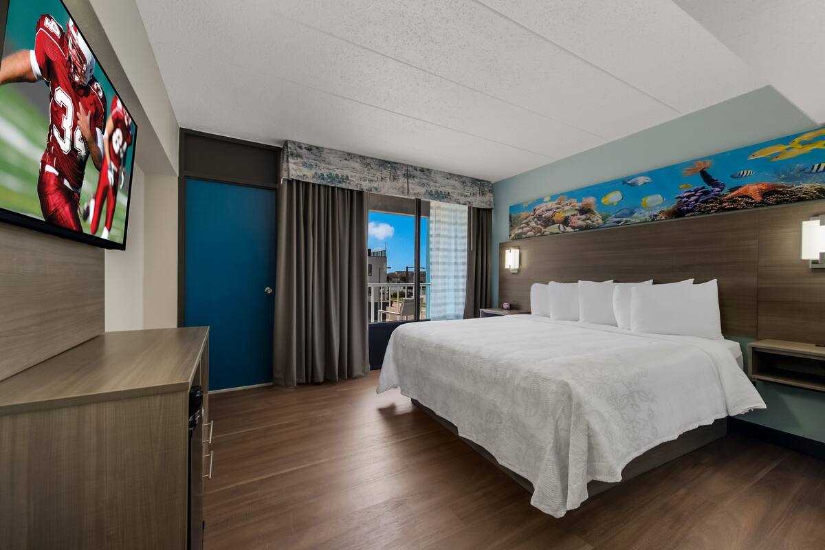 Una habitación de hotel con cama, televisión, un mural y vista a la ciudad.