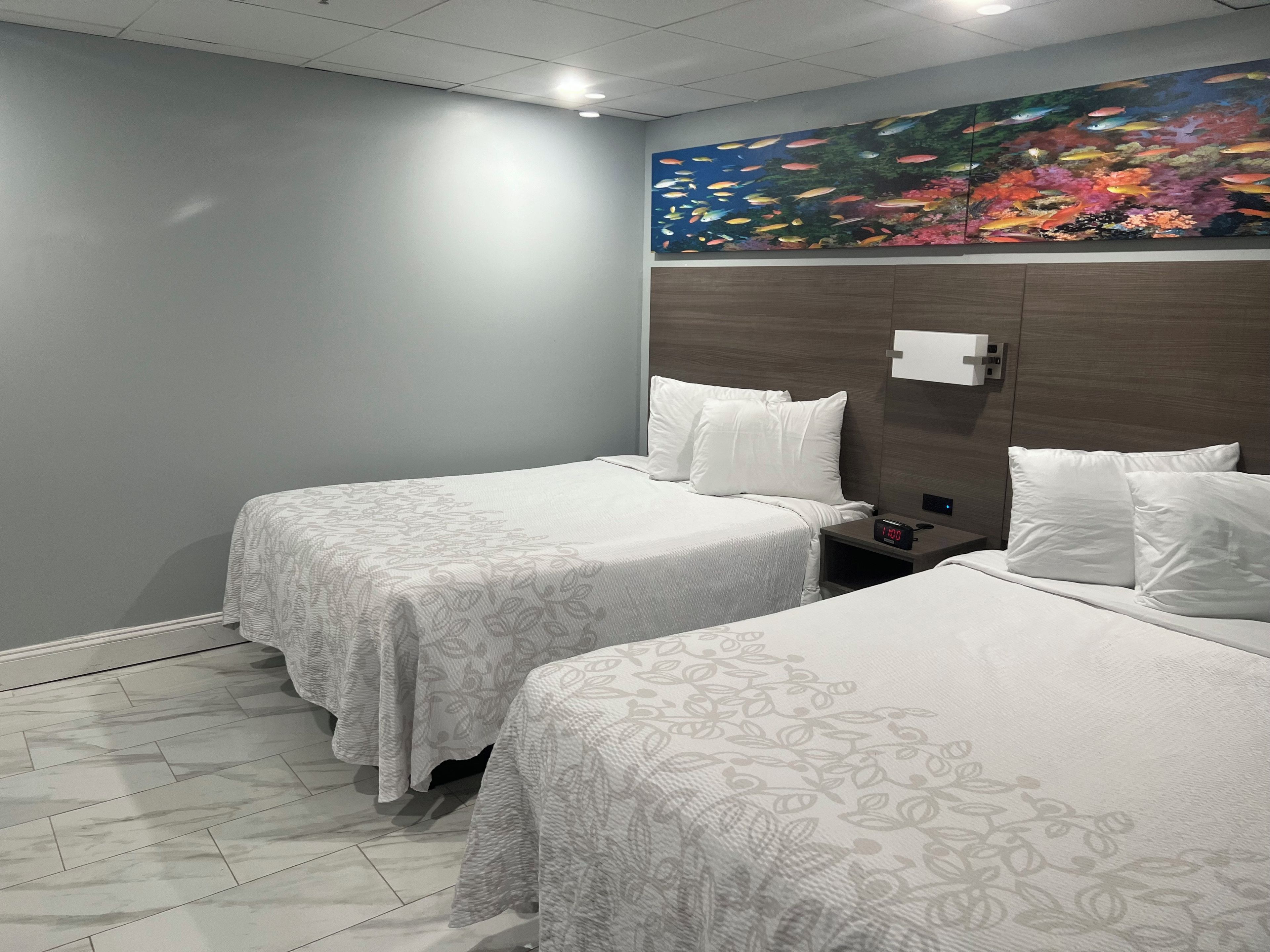 Quarto de hotel com duas camas, uma mesa de cabeceira, um relógio digital e um quadro grande na parede.