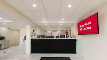 A hotel reception area with a Red Roof Plus+ sign, a Red Roof Plus+ sign on the wall, and a Red Roof Plus+ sign on the floor mat.