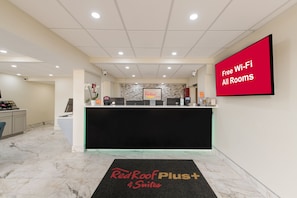 A hotel reception area with a Red Roof Plus+ sign, a Red Roof Plus+ sign on the wall, and a Red Roof Plus+ sign on the floor mat.