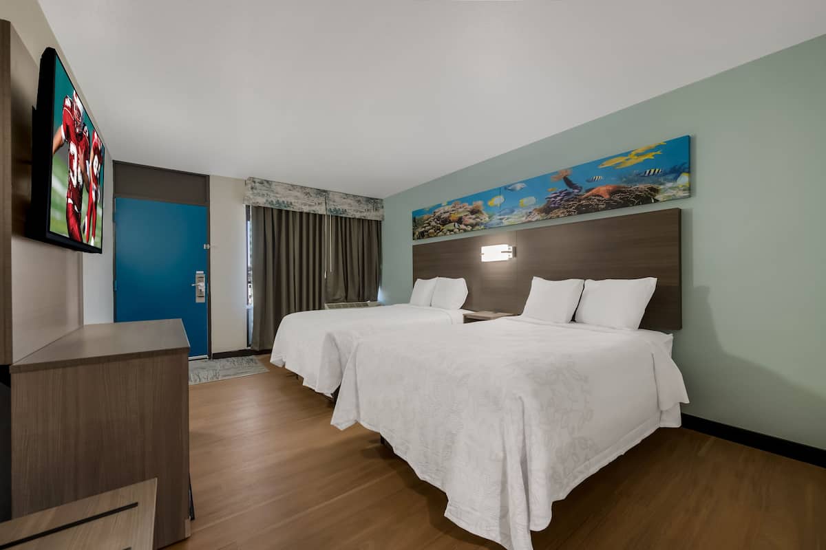 Habitación de hotel con dos camas, un escritorio, un televisor y un cuadro en la pared.