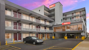 A multi-story hotel with a parking lot, a sign for Red Roof Plus & Suites, and a black car parked in the lot.