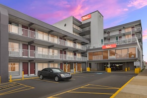 A multi-story hotel with a parking lot, a sign for Red Roof Plus & Suites, and a black car parked in the lot. - Red Roof Inn PLUS+ & Suites Virginia Beach – Seaside (Virginia Beach)