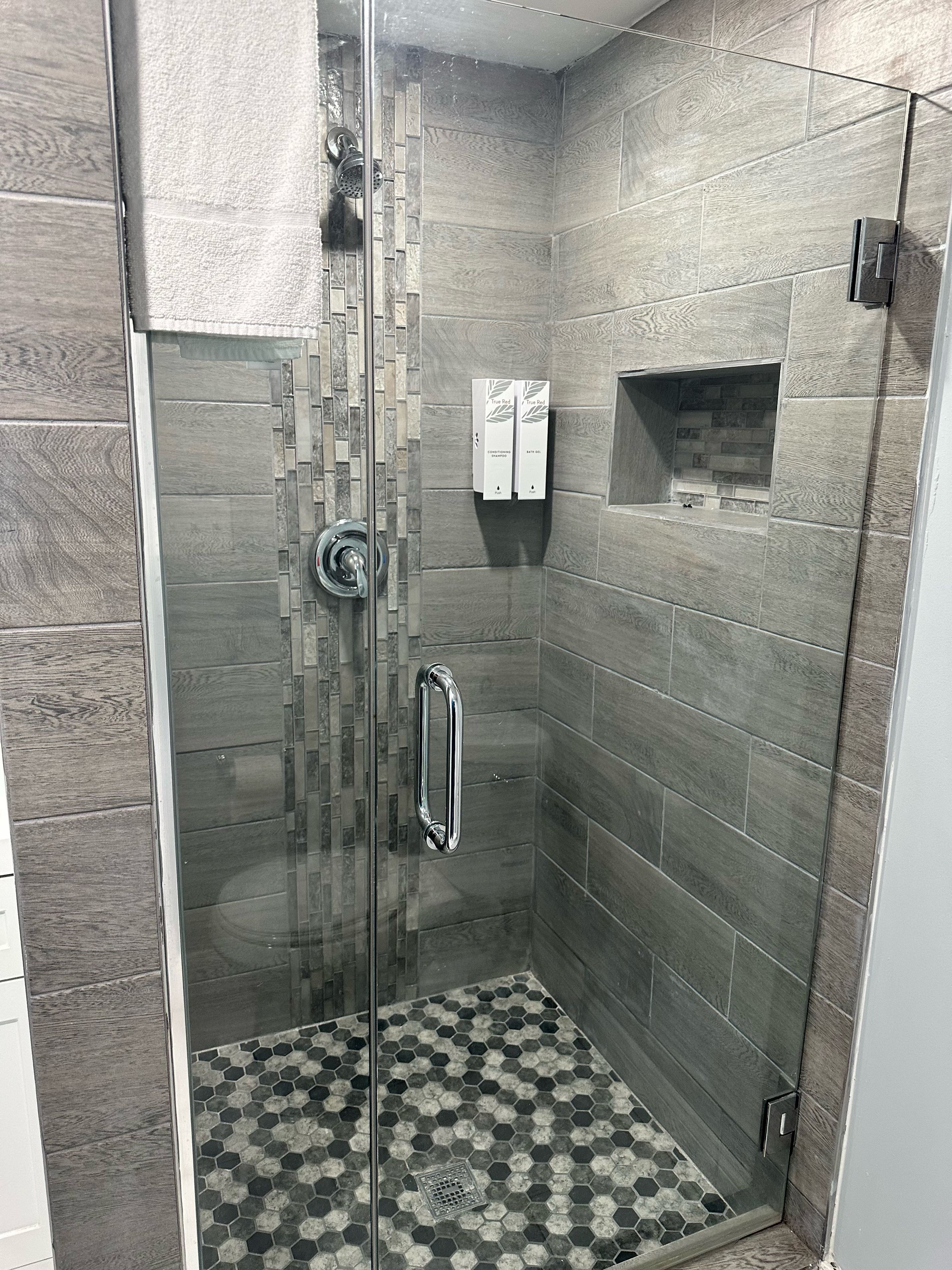 Ducha con puerta de cristal, barra de apoyo y suelo de baldosas con diseño geométrico.