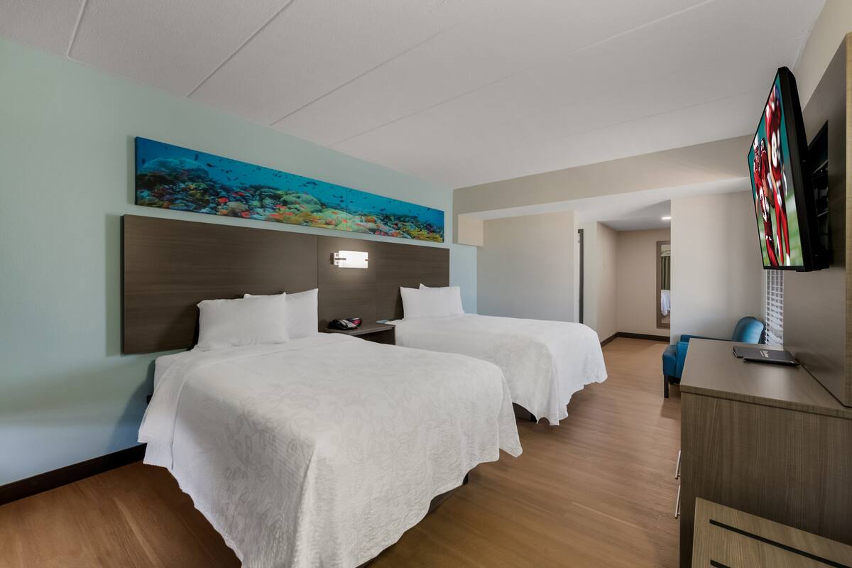 Habitación de hotel con dos camas, un televisor de pantalla plana, un cuadro de una escena submarina y un escritorio de madera.