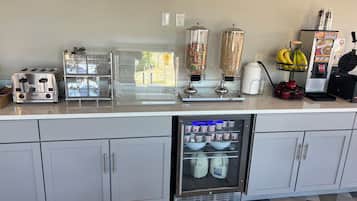 A kitchenette with a toaster, a blender, a refrigerator, and a fruit basket.
