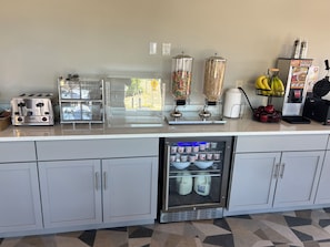 A kitchenette with a toaster, a blender, a refrigerator, and a fruit basket.
