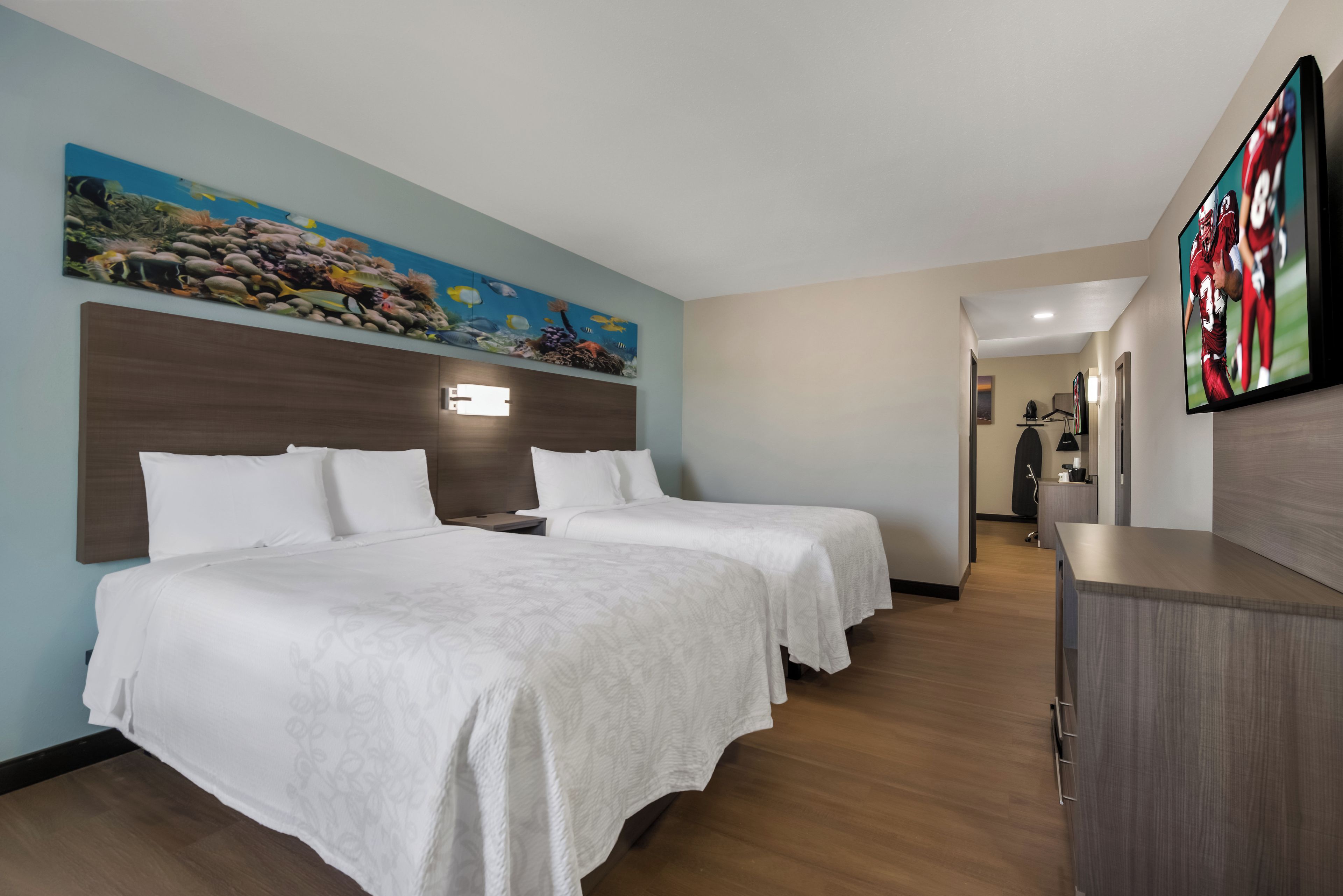 Habitación de hotel con dos camas, un cuadro de una escena submarina y un televisor en la pared.
