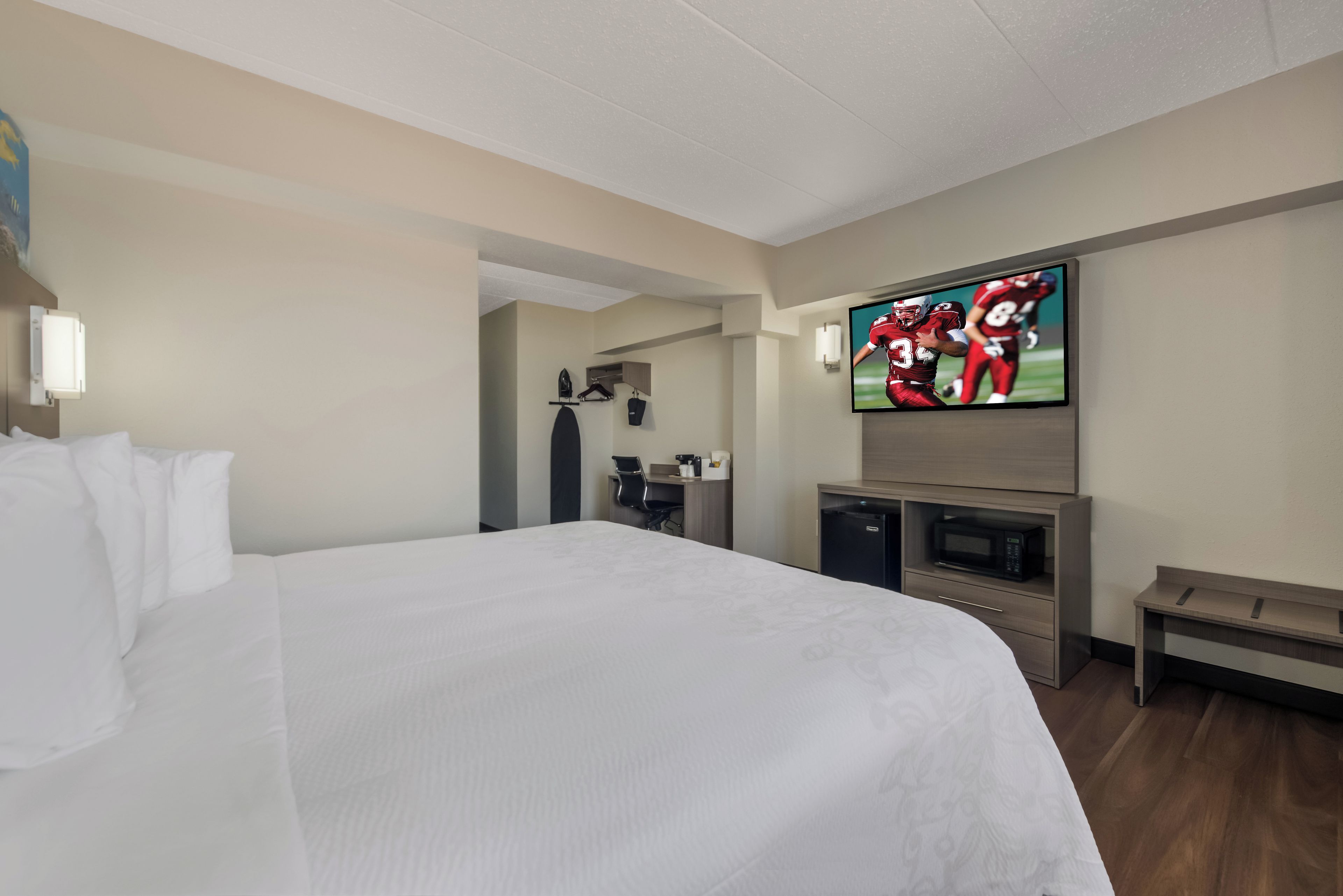 Ein Hotelzimmer mit einem großen Bett, einem flachbildfernseher an der Wand, einem kleinen Schreibtisch mit einer Mikrowelle und einer Bank.
