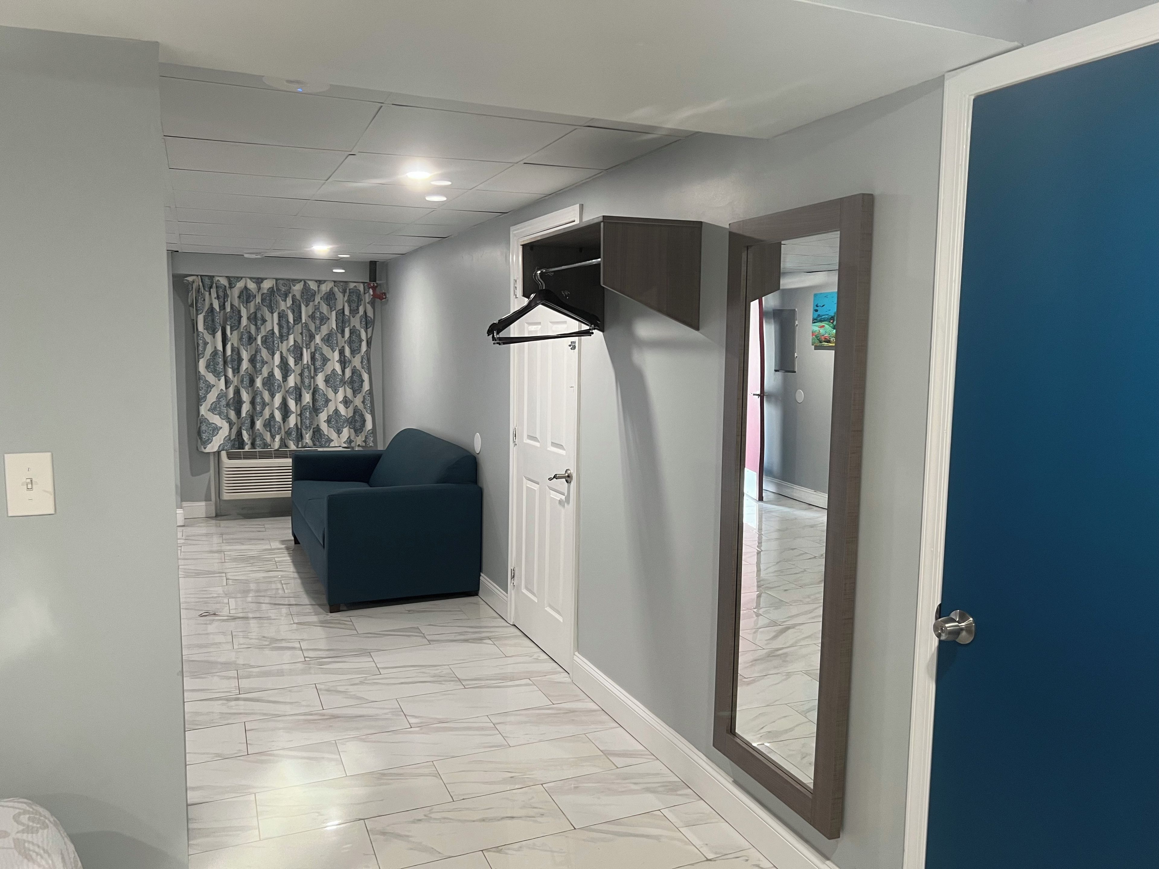 A hallway with a blue door, a dark blue sofa, a white door, and a patterned curtain.