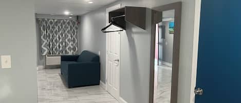 Un pasillo con una puerta azul, un sofá azul oscuro, una puerta blanca y una cortina estampada.