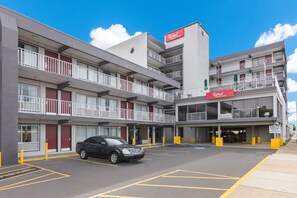 A multi-story hotel with a parking area and a black car parked in the lot. - Red Roof Inn PLUS+ & Suites Virginia Beach – Seaside (Virginia Beach)
