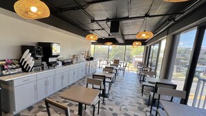 A modern cafe with a long counter, seating area, and large windows offering a view. - Red Roof Inn PLUS+ & Suites Virginia Beach – Seaside (Virginia Beach)
