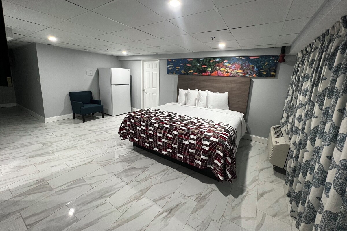 A hotel room with a bed, a chair, a refrigerator, and a shower area.