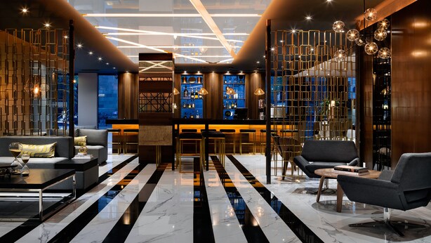 A modern lobby with a black and white striped floor, a bar area with shelves of bottles, and a seating area with sofas and tables. - SENS Hotel (Montreal)