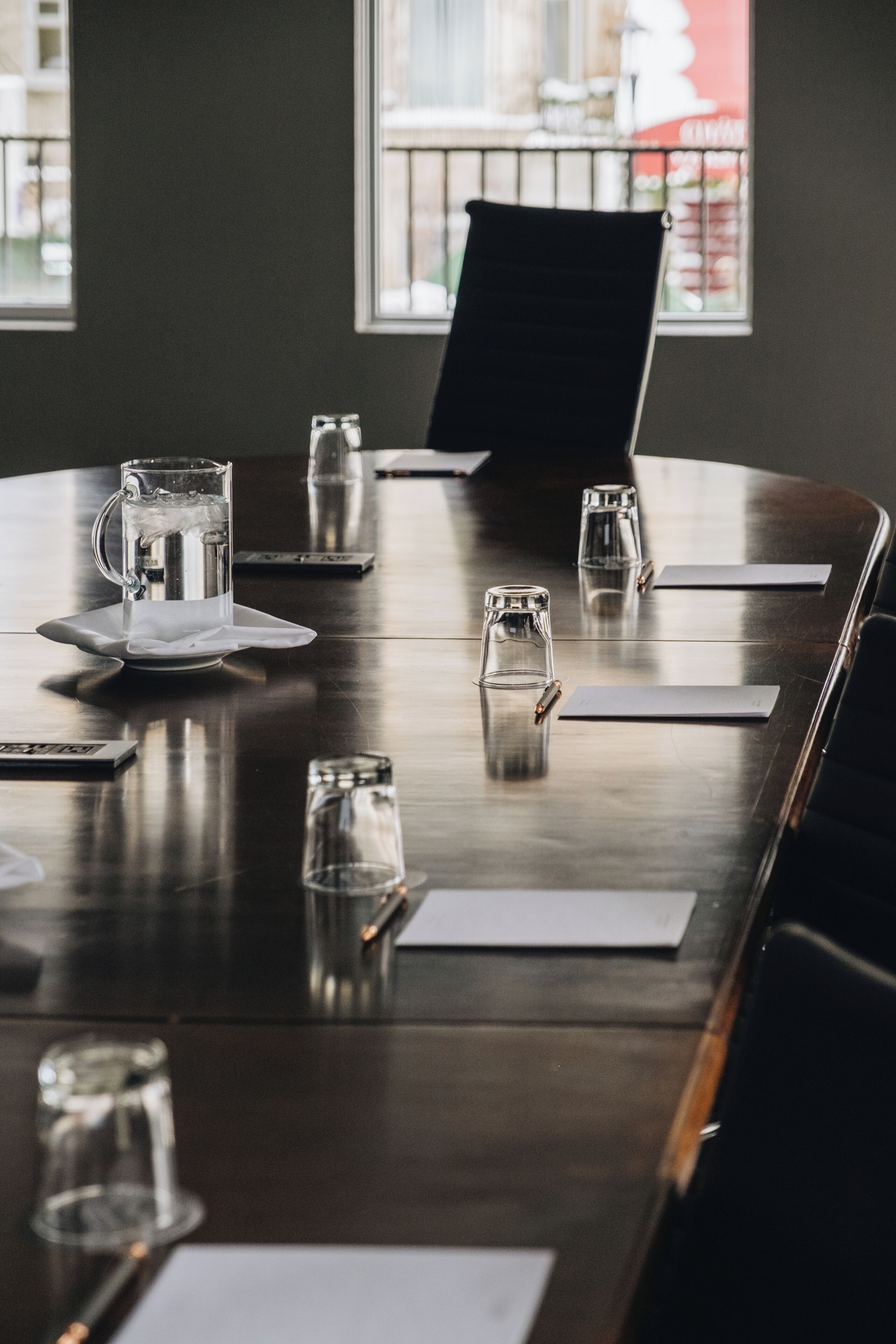 A conference table with water glasses, a pitcher, and documents, set against a dark wall with a window.