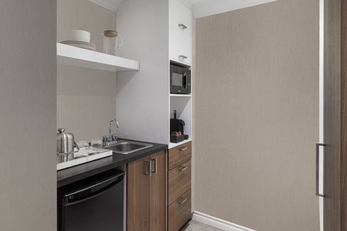A modern kitchen with a built-in dishwasher, a microwave, and a coffee maker on a white shelf.