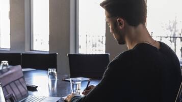 A person seated at a table with a laptop, writing, and a glass of water.