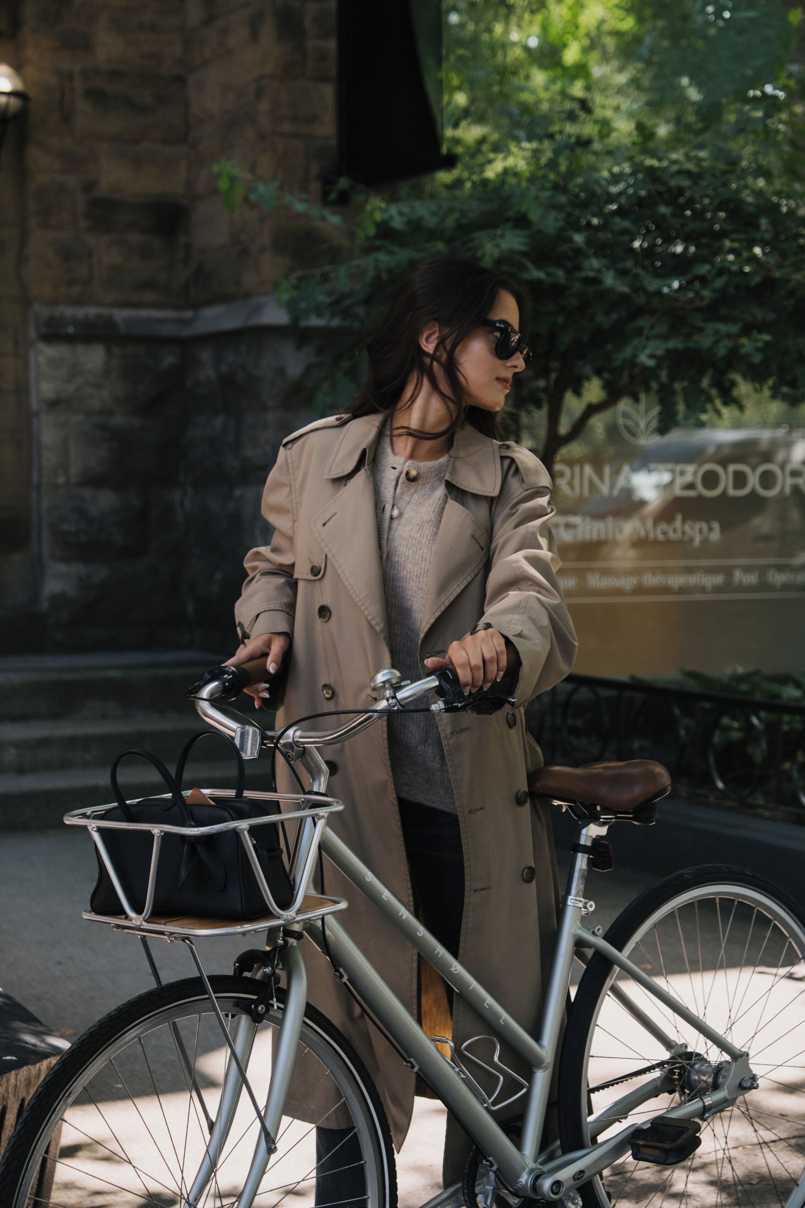 A person standing next to a bicycle with a basket, in front of a building with a sign.