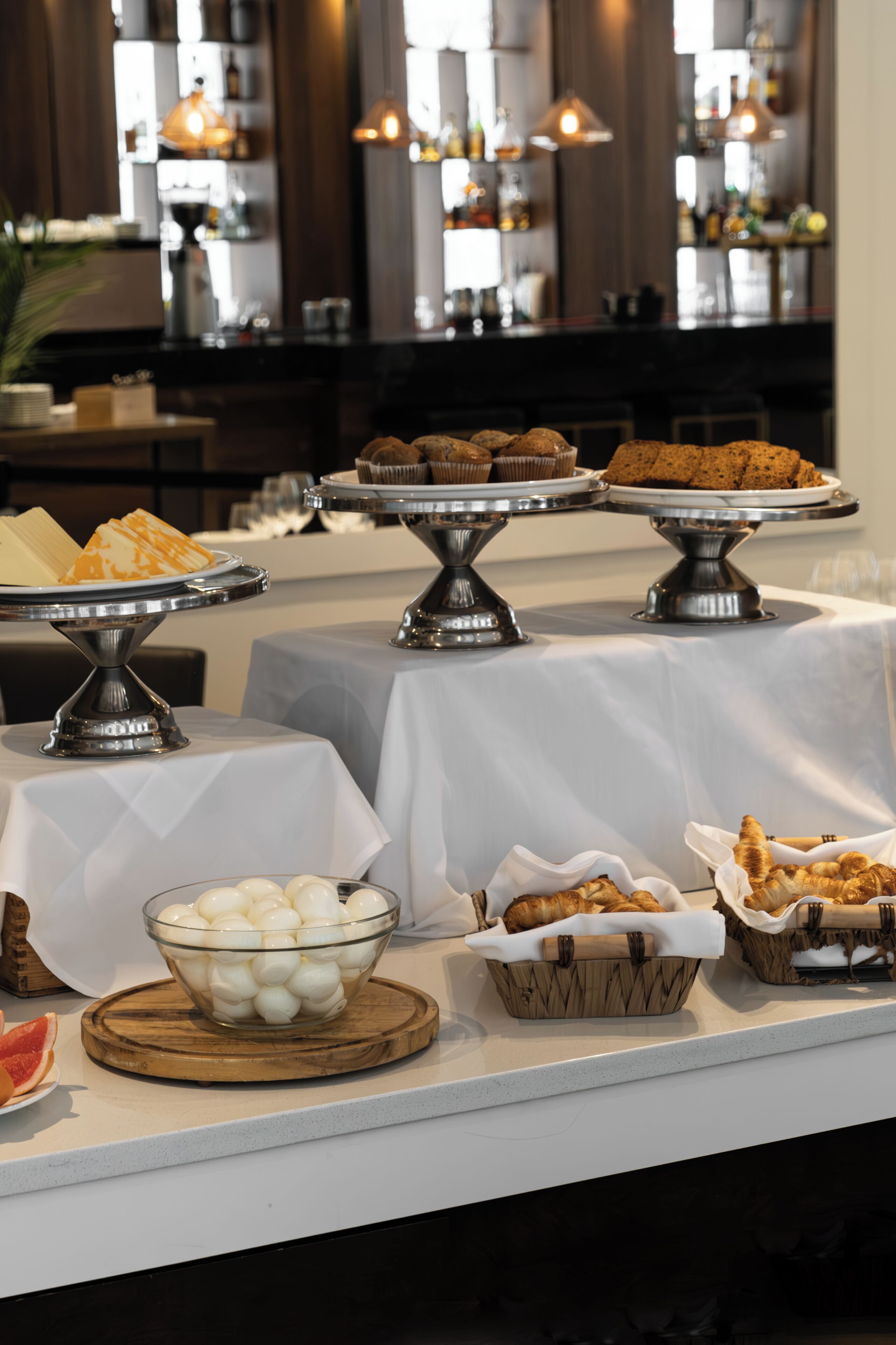 Une table de buffet proposant divers plats, notamment des pâtisseries, du pain et un saladier d’œufs.