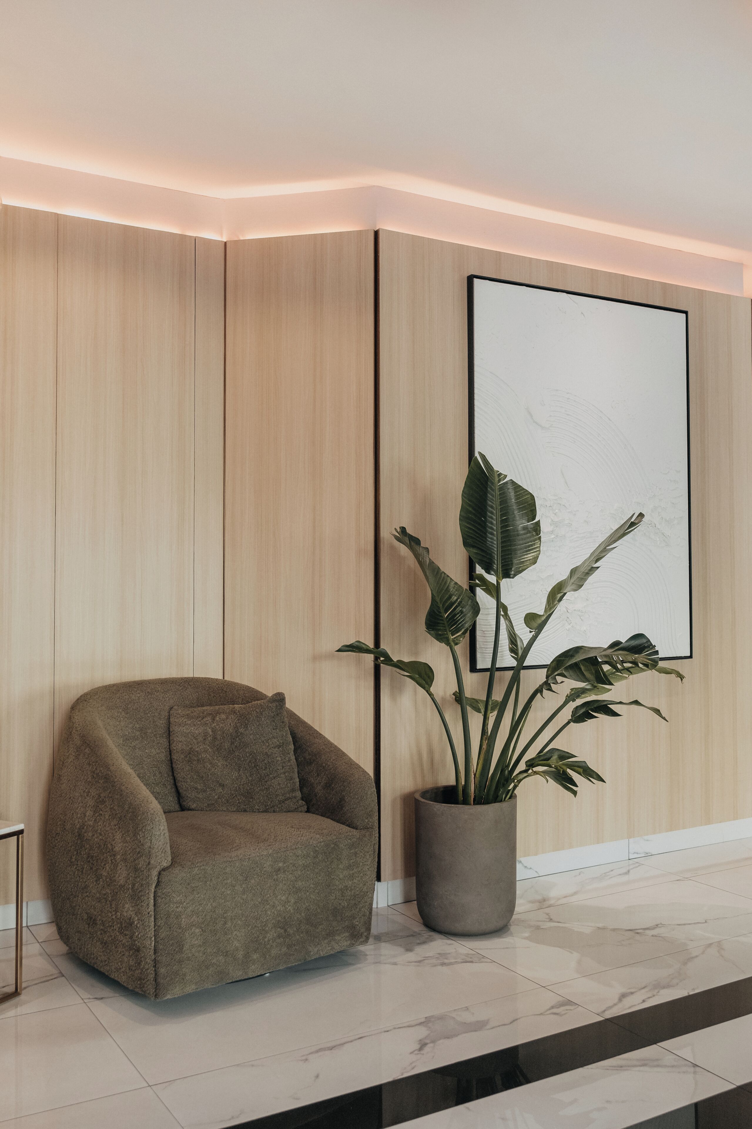A modern lobby with a cushioned armchair, a potted plant, and a large abstract painting on the wall.