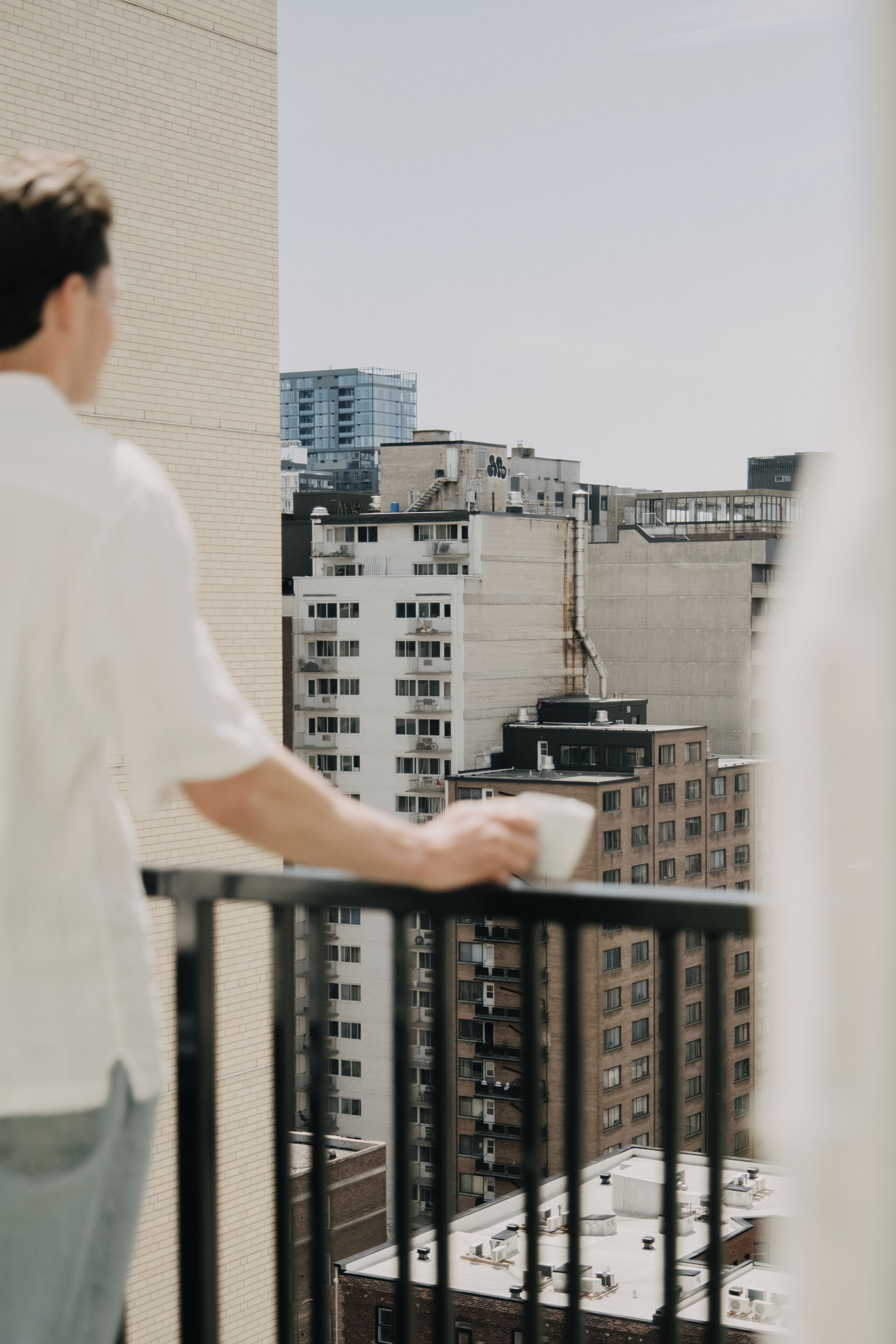 Iemand staat op een balkon met uitzicht op hoge gebouwen.