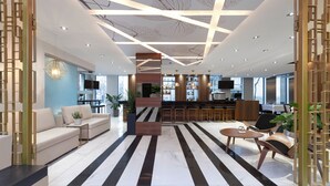 A modern hotel lobby with a striped floor, a sofa, a coffee table, and a bar area with a TV. - SENS Hotel (Montreal)
