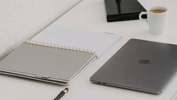 A white desk with a laptop, a notebook, a pen, a lamp, and a cup of coffee.