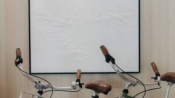 Dos bicicletas con asientos de madera y cestas de metal, estacionadas frente a una obra de arte colgada en la pared.