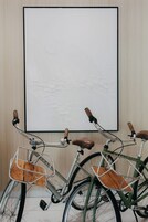 Two bicycles with wooden seats and metal baskets, parked in front of a wall-mounted artwork.