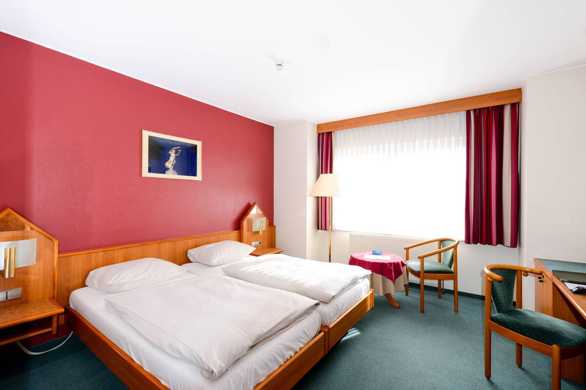 A hotel room with two beds, a desk, a chair, and a window with curtains.
