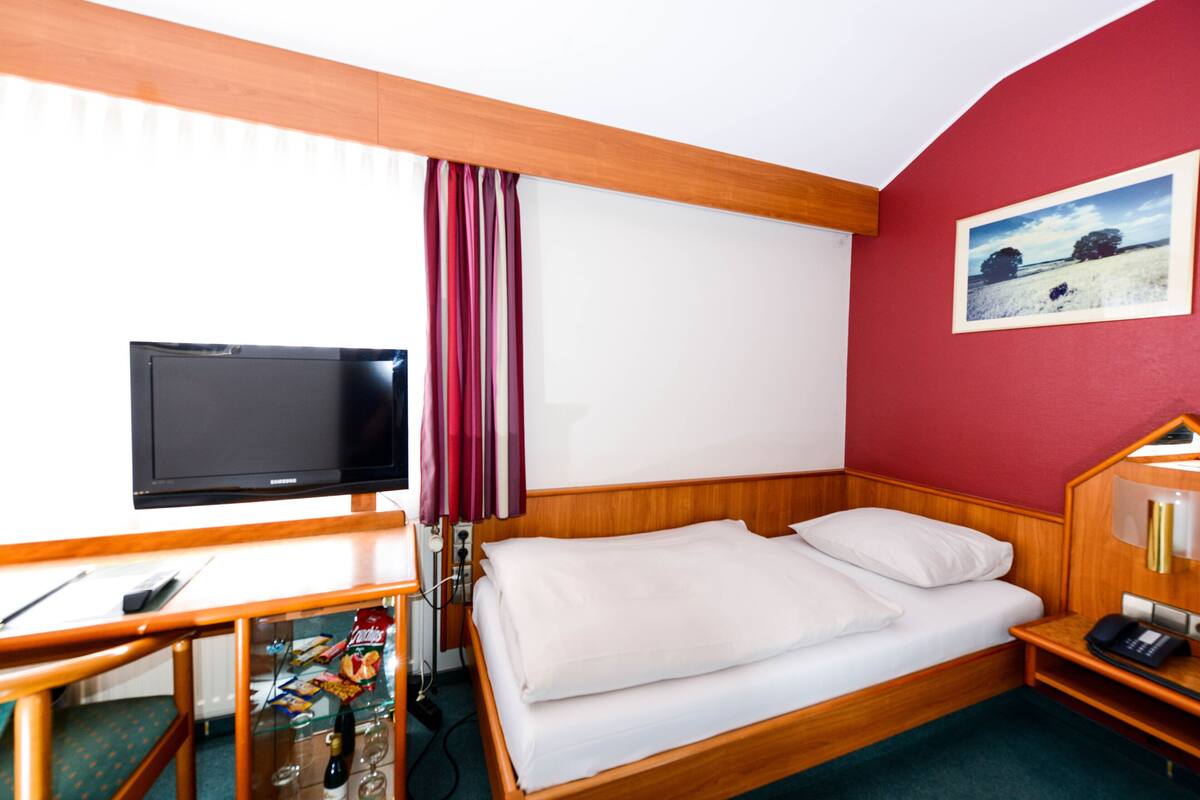 A hotel room with a wooden bed, a television, a desk with a chair, and a painting on the wall.