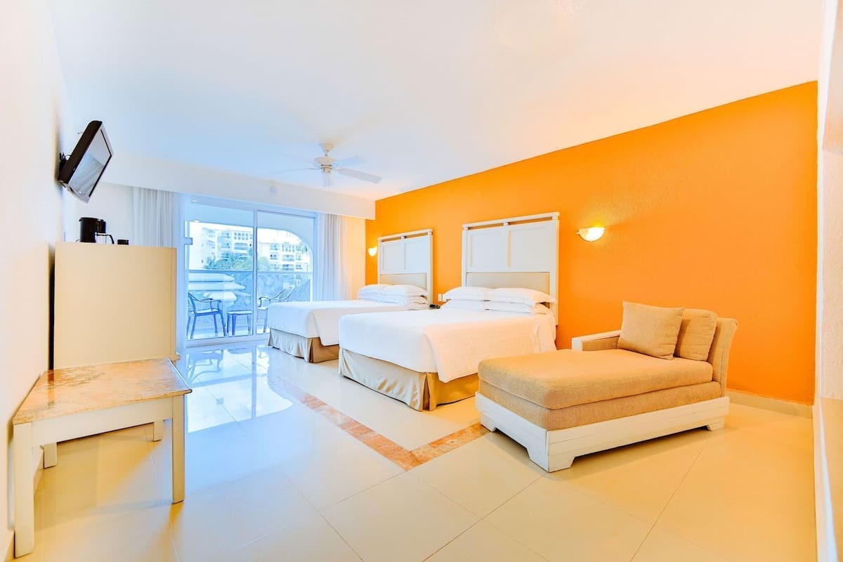 Una habitación de hotel con dos camas, un sofá, un televisor y un balcón con mobiliario exterior.