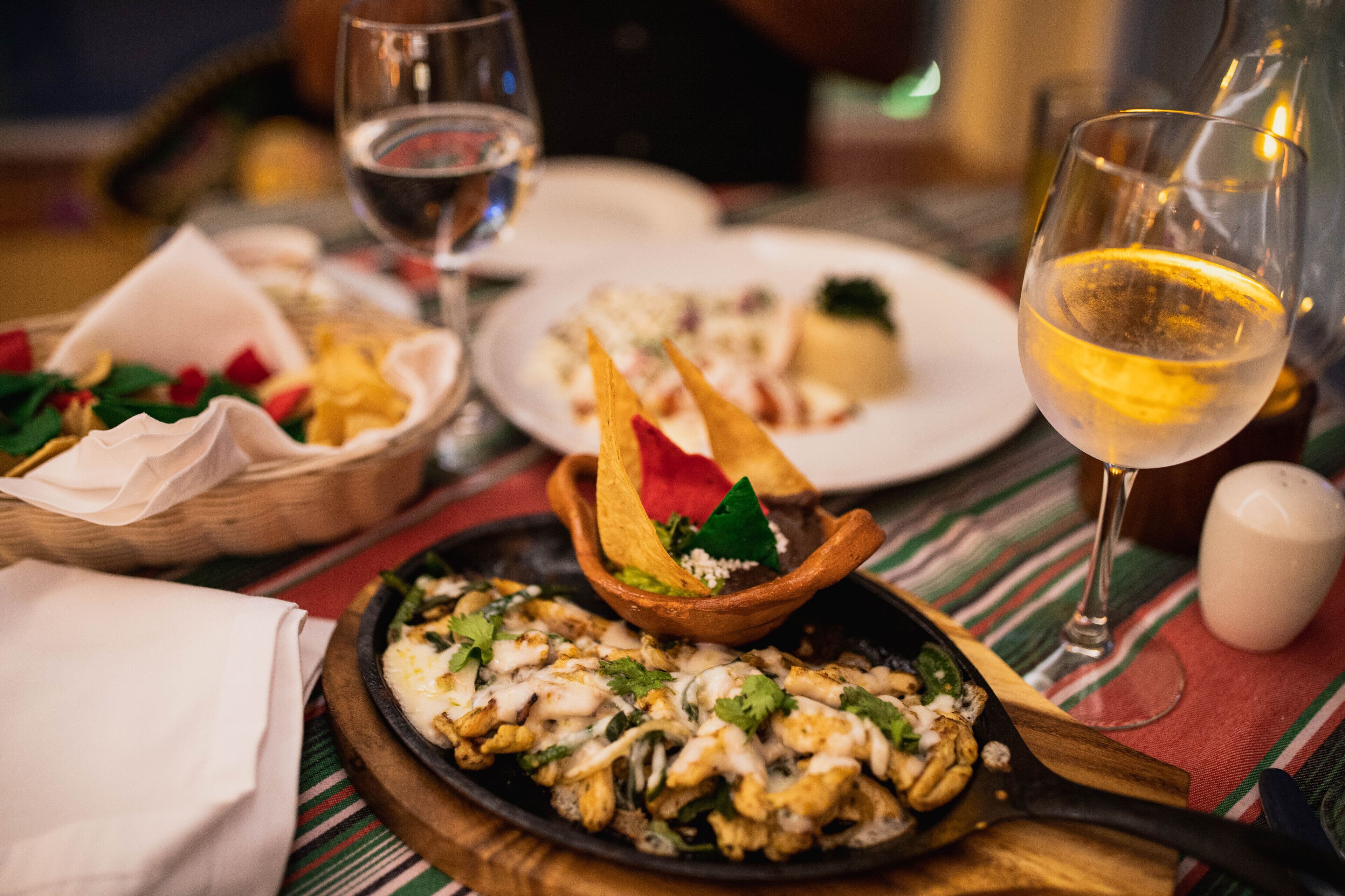 A dining table with a variety of dishes, including a skillet with food, plates with different dishes, and glasses of wine.