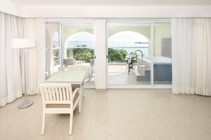 Habitación de hotel con balcón, zona de comedor con mesa y sillas, y vista al océano.