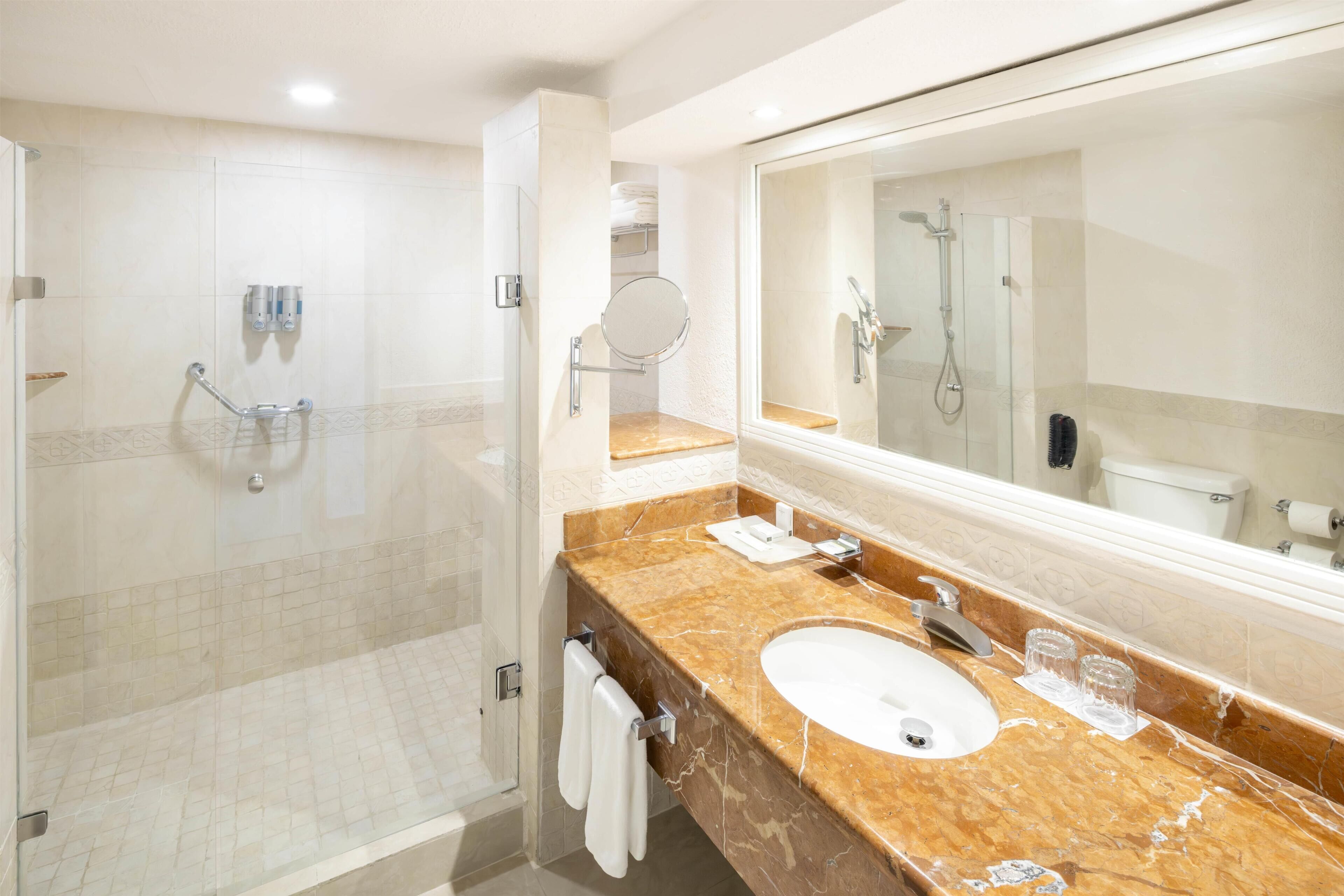 A modern bathroom with a glass-enclosed shower, a marble sink, and a large mirror.