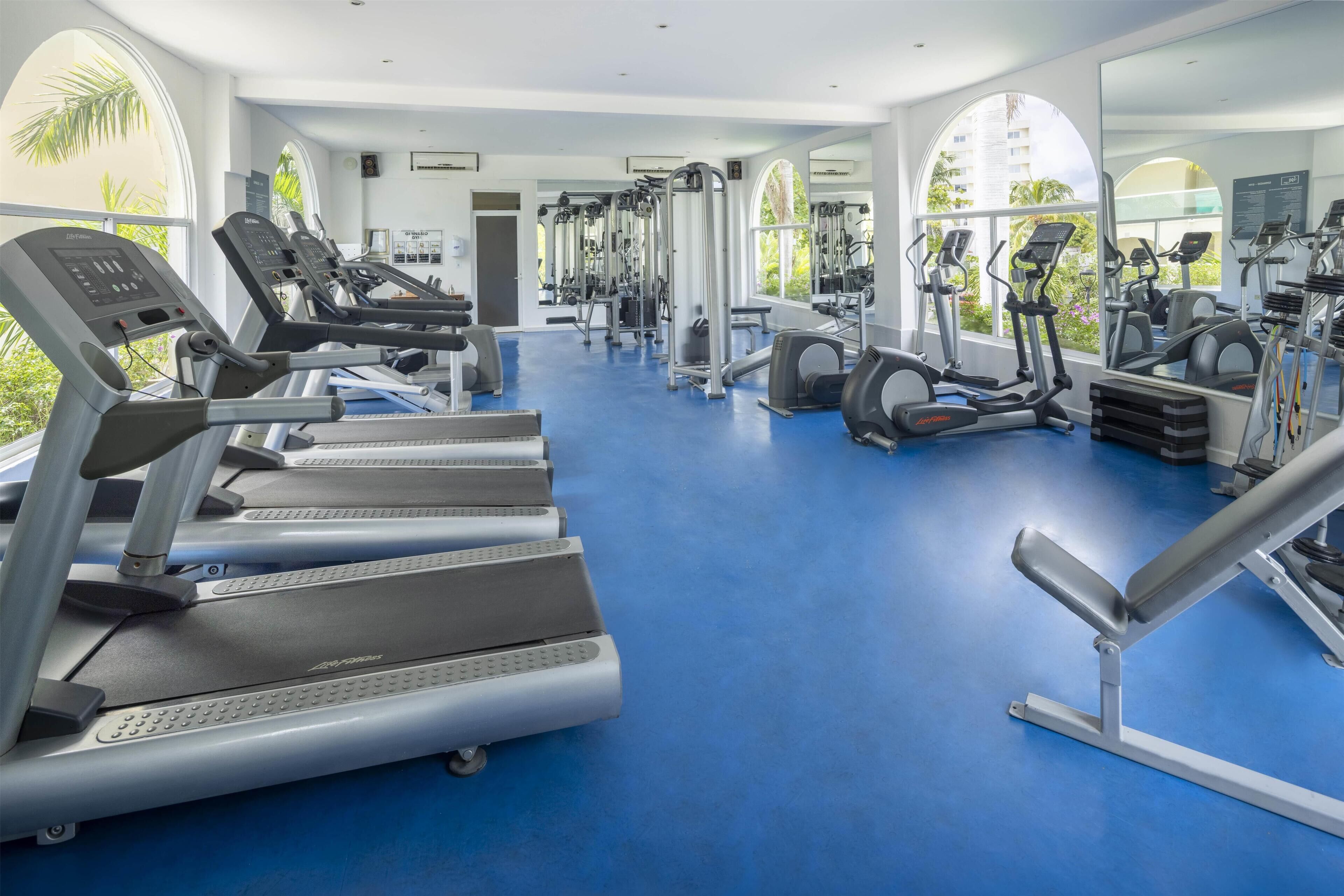 Un gimnasio con cintas de correr, elípticas y equipo de pesas.