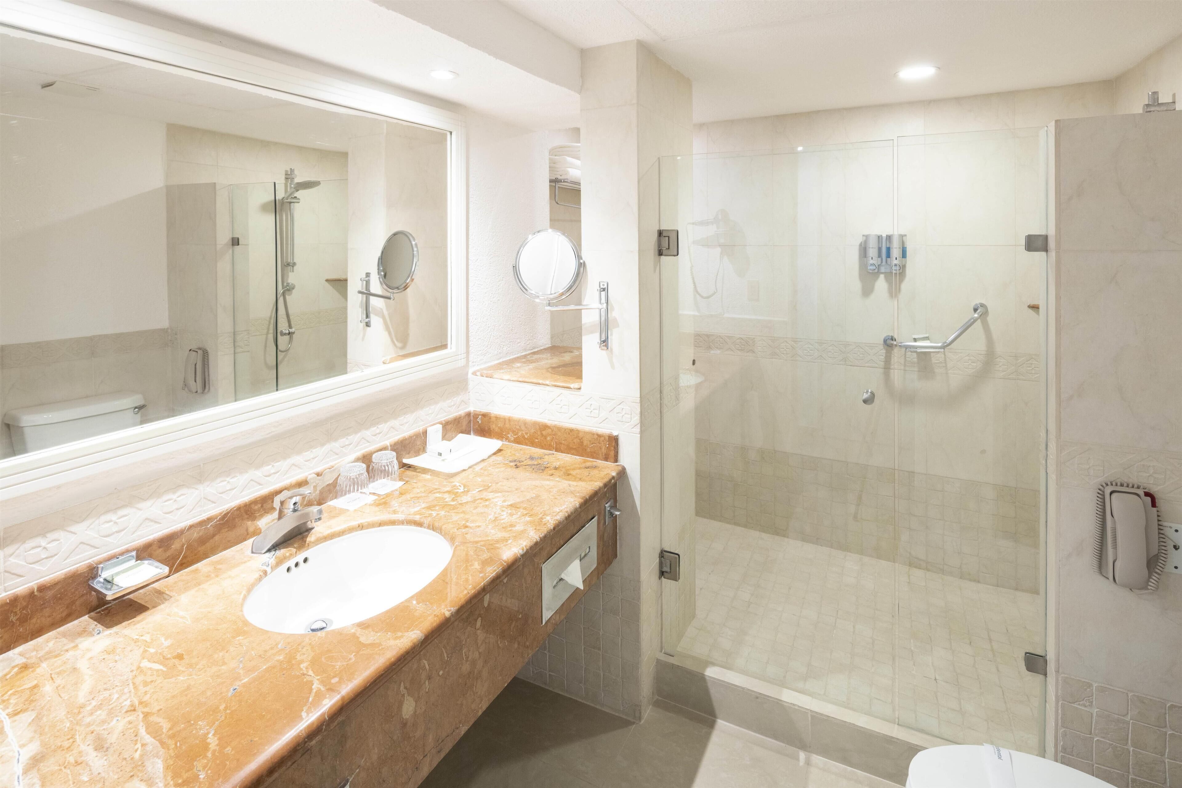 Un baño moderno con lavamanos de mármol, un espejo grande, una ducha con mampara de vidrio y un inodoro.