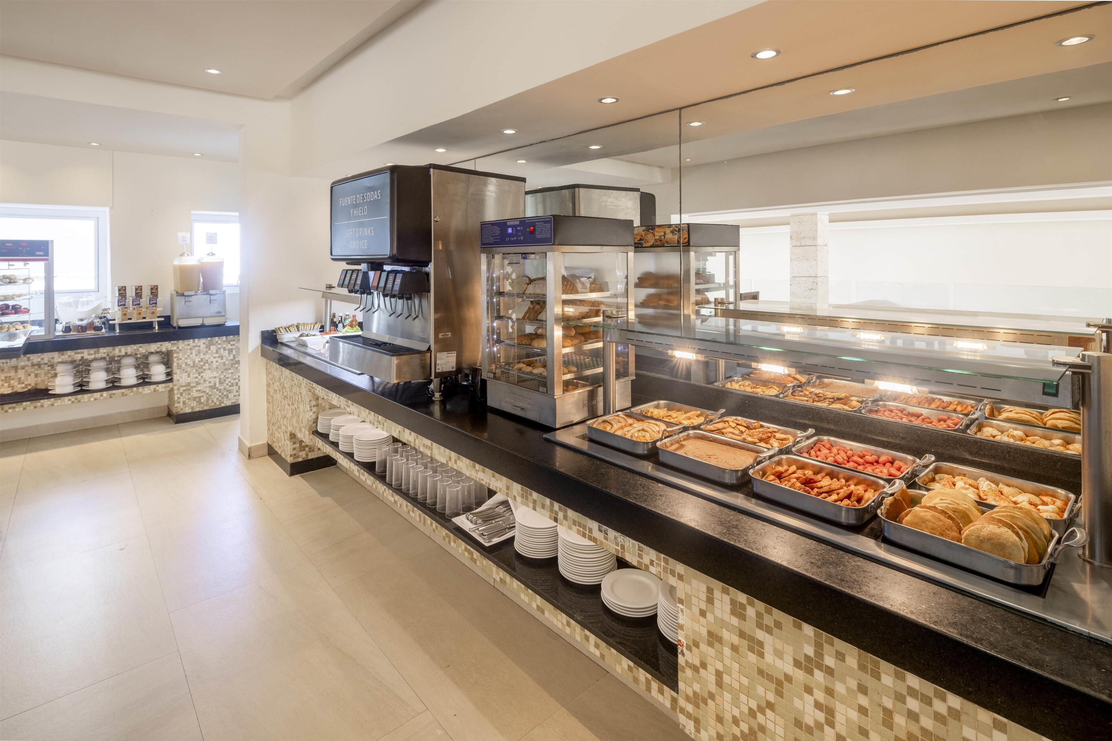 Un'area buffet con una macchina da caffè, diversi vassoi con cibo e una vetrina in vetro.