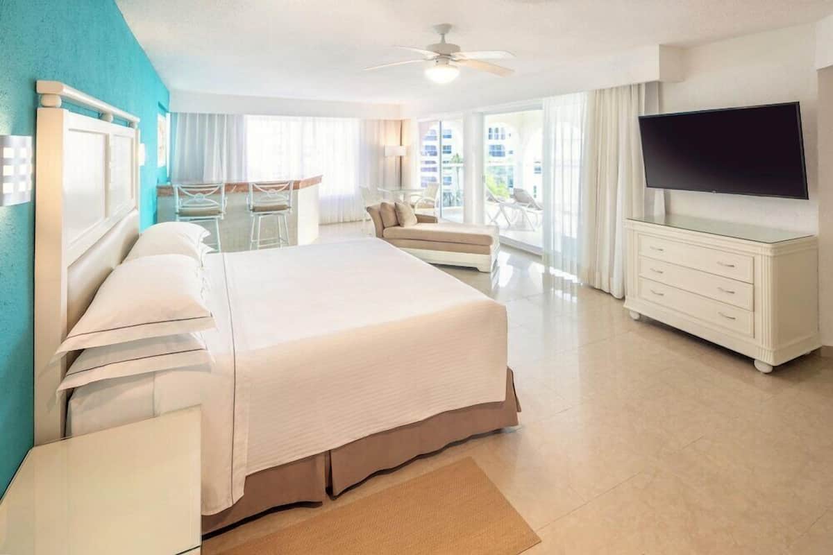 Habitación de hotel con una cama grande, televisión, escritorio y balcón con sillas.