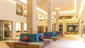 Eine geräumige Lobby mit mehreren Sitzbereichen, großen Säulen und einer hohen Decke.