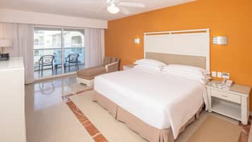 A hotel room with a bed, a desk, a chair, a balcony with chairs, and a ceiling fan.