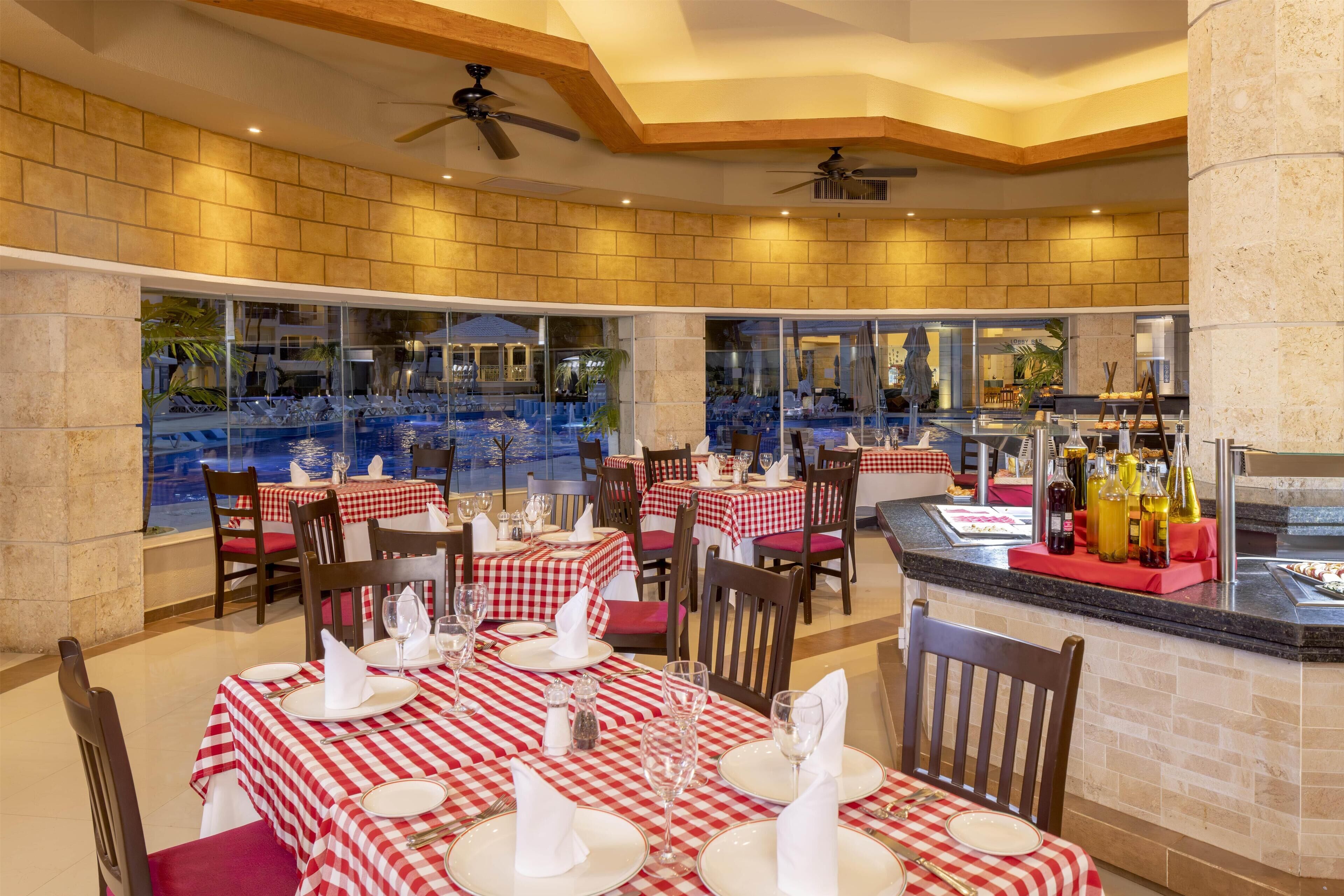 A restaurant with checkered tablecloths, wooden chairs, and a pool view.
