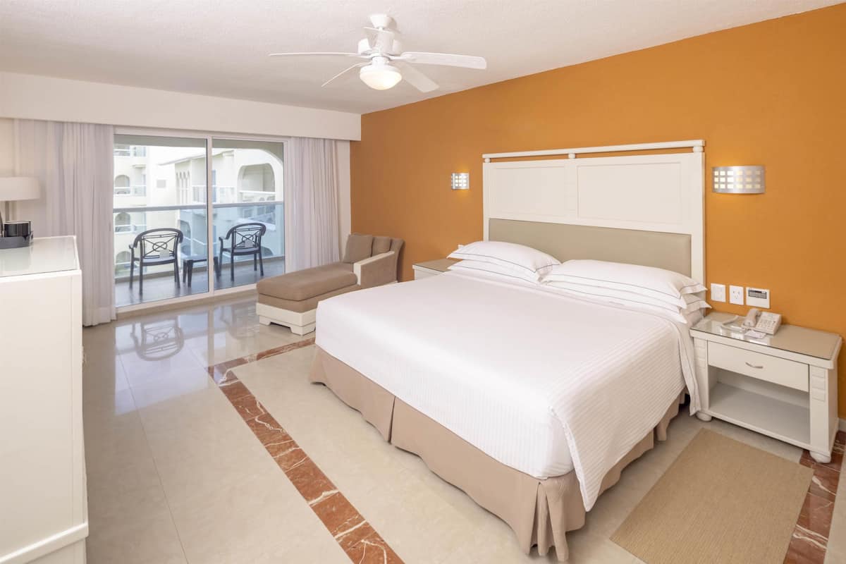 Habitación de hotel con una cama grande, un escritorio, una silla y un balcón con sillas.